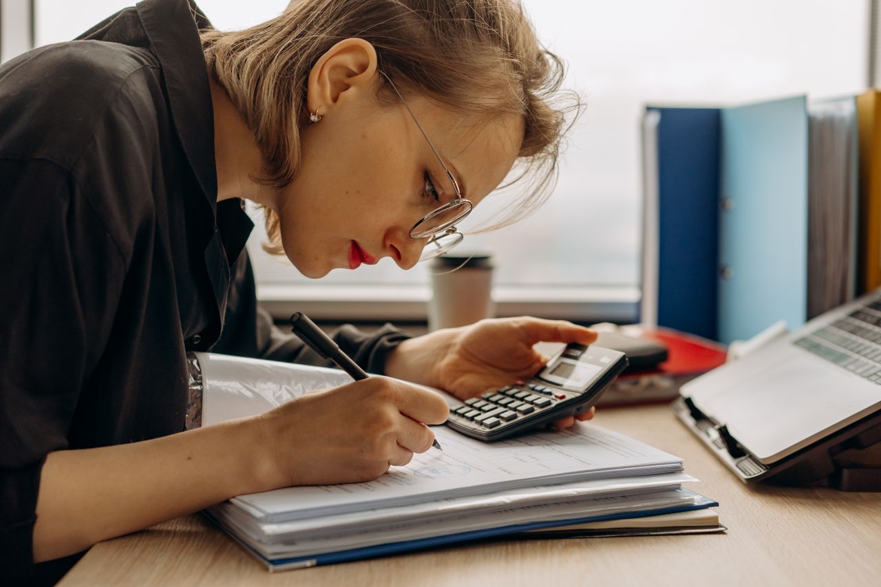 services-05 Young woman diligently working on accounting with a calculator and documents. Perfect for business and finance themes.