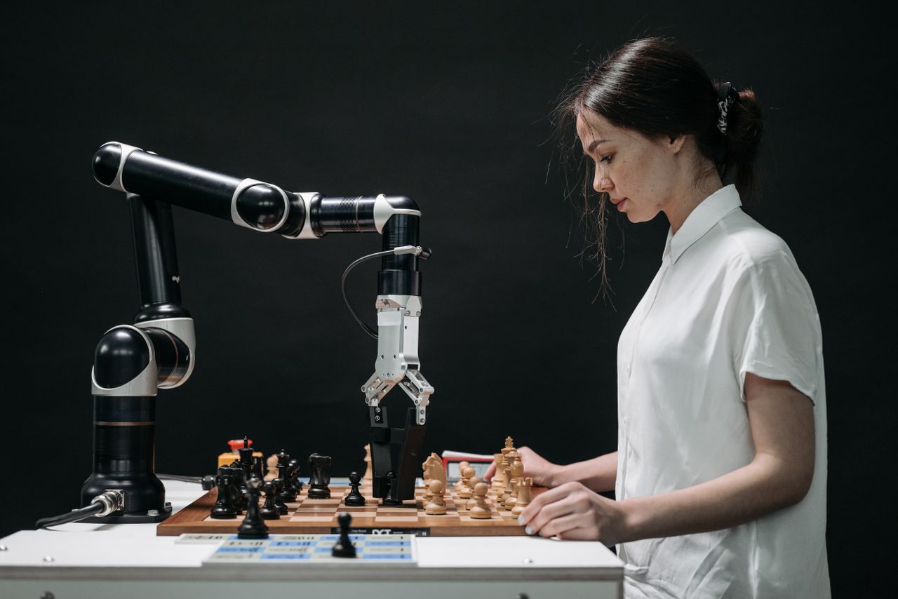 about-us A robot and woman engage in chess, showcasing technology and strategic thinking.